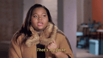 Person confidently saying, &quot;That&#x27;s my forte,&quot; in an indoor setting. They wear a fur-lined cape