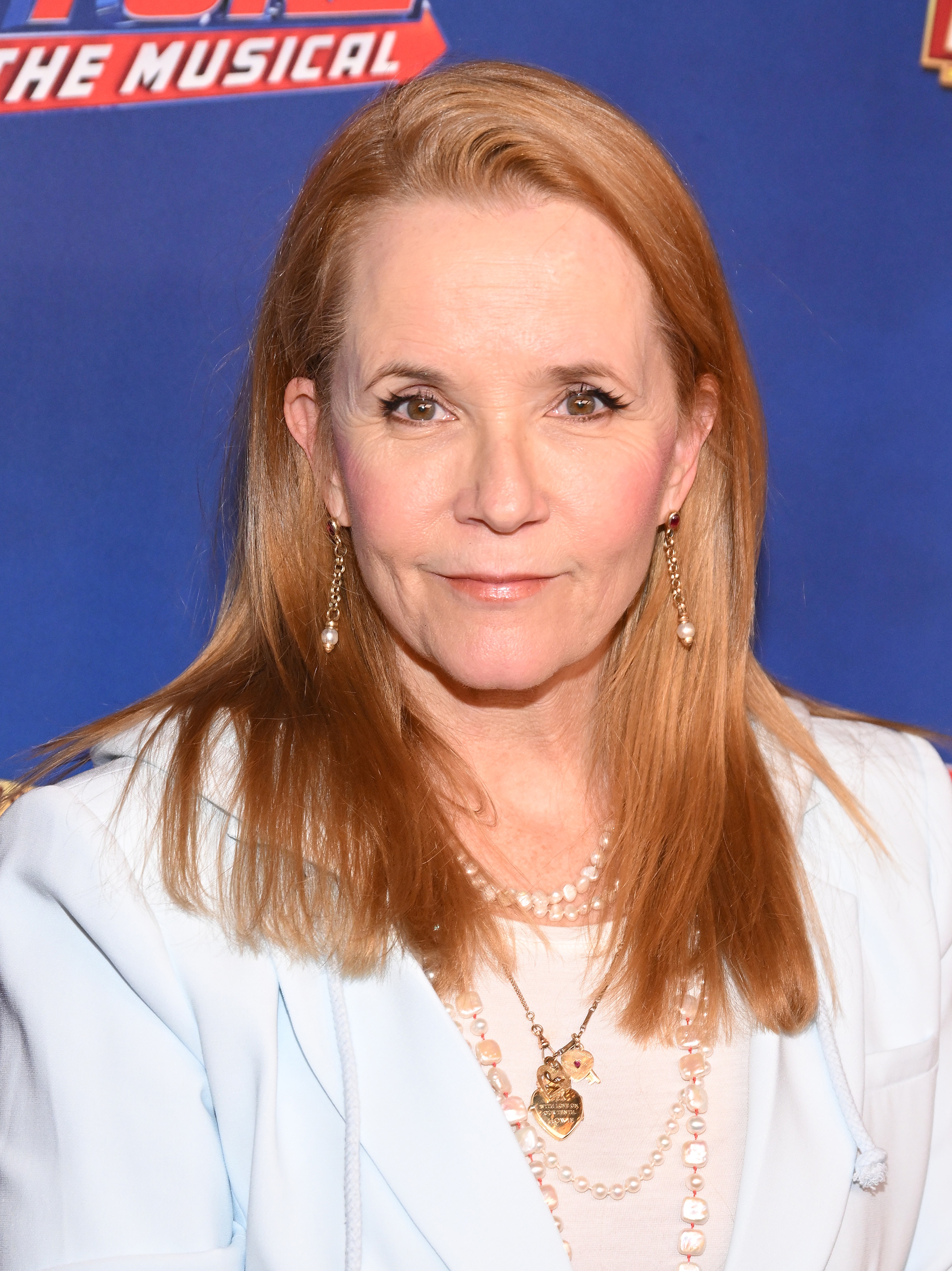Person in elegant attire with pearl necklace at a media event backdrop