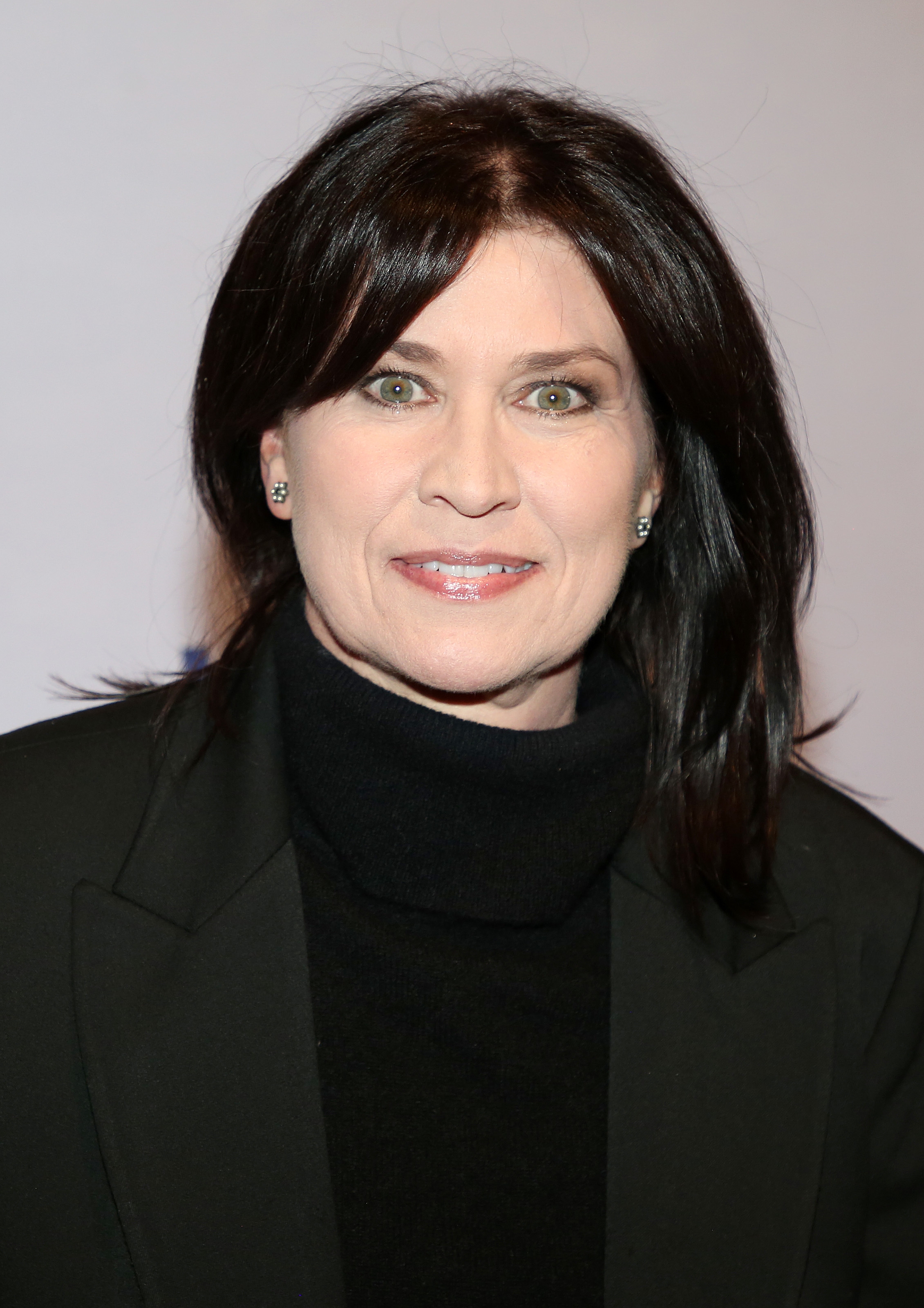 Person in a black turtleneck and blazer at a celebrity event, smiling at the camera