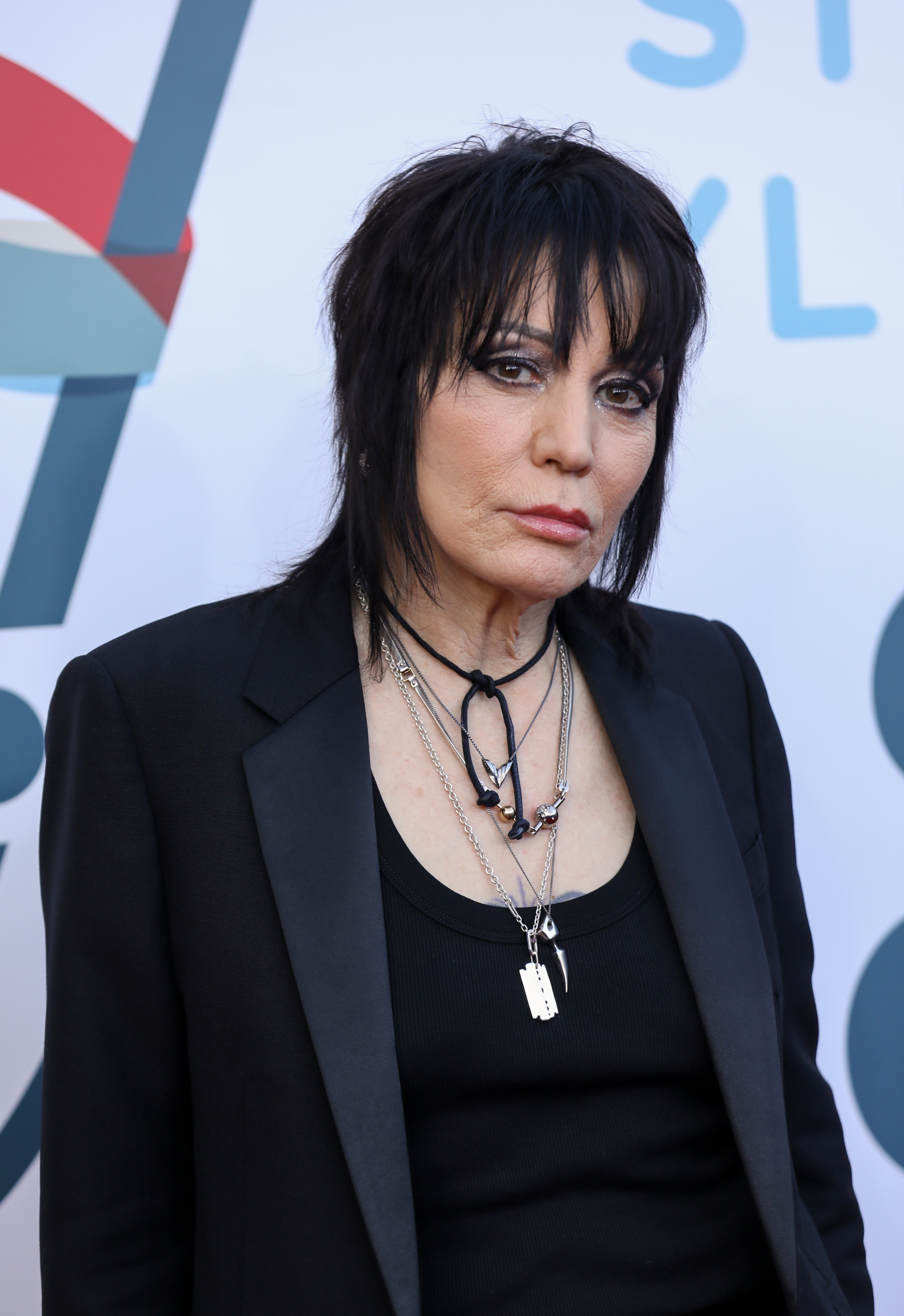 A person in a black blazer and layered necklaces with a confident expression, at a celebrity event