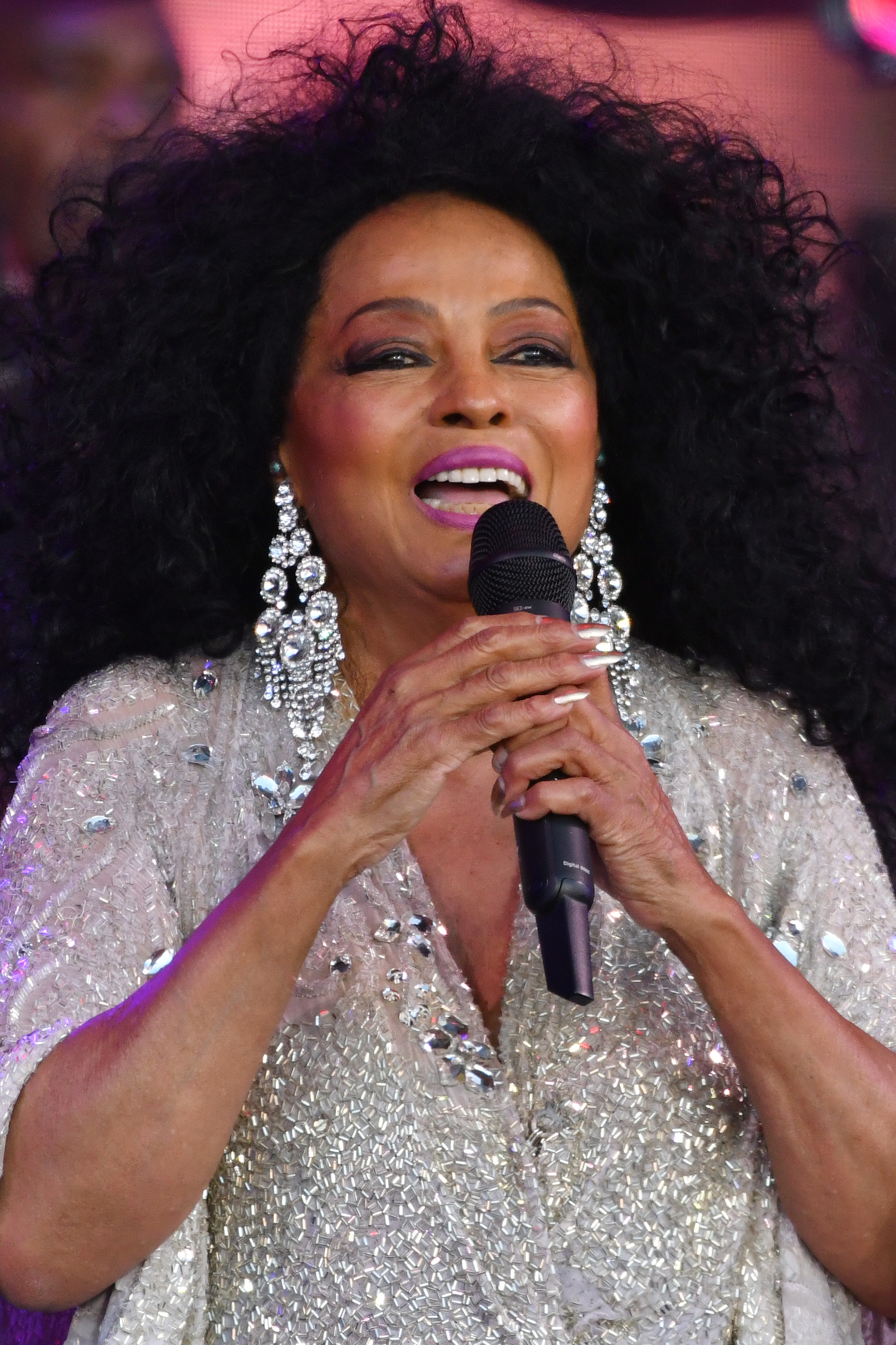 Singer in sparkling top and statement earrings performs, holding a microphone with a joyful expression onstage