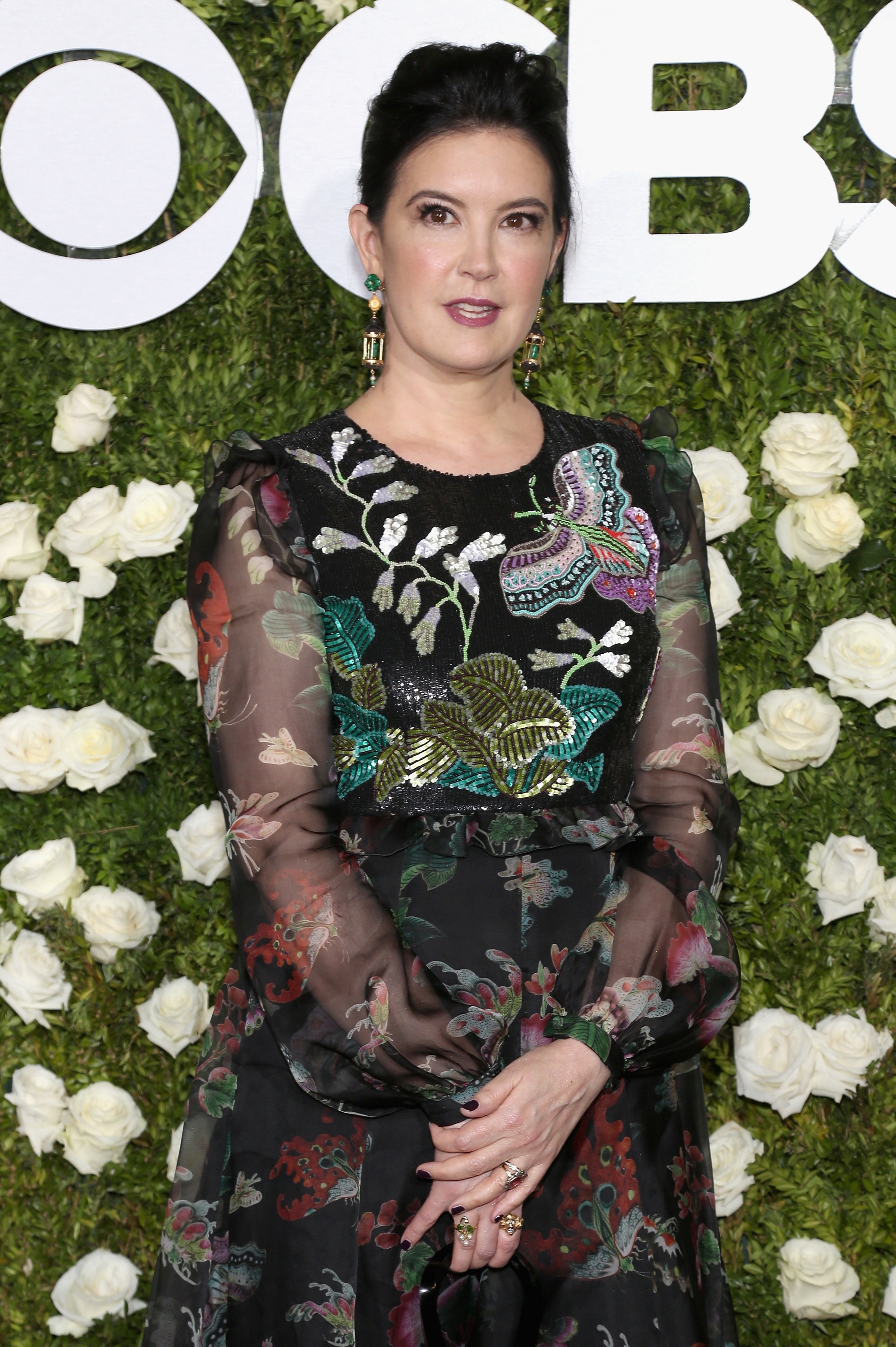 Person in a floral-print dress with sheer sleeves at a CBS event, standing in front of a floral backdrop