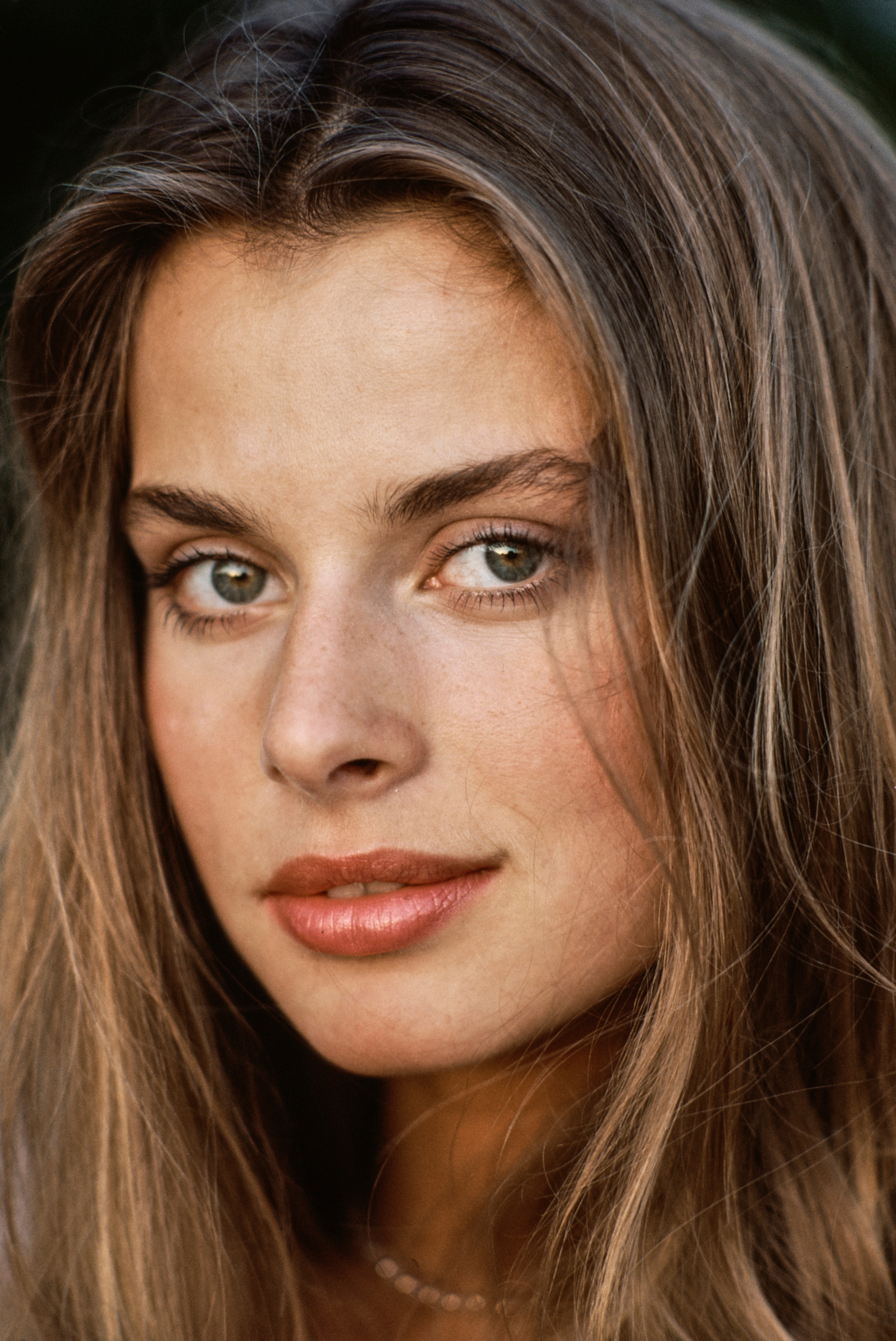 A person with long hair looks directly at the camera with a neutral expression
