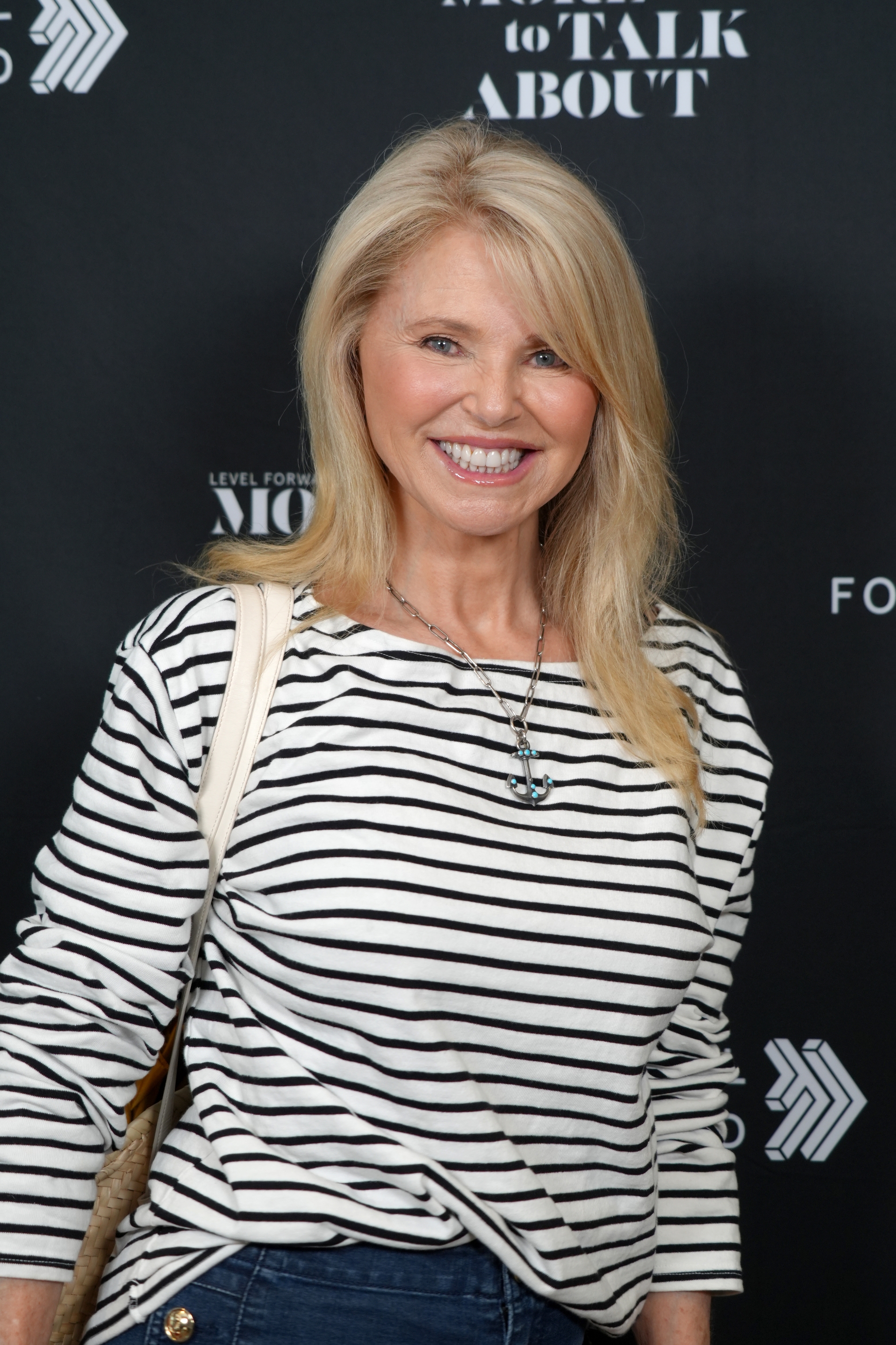 Person smiling, wearing a striped top and jeans, standing in front of a promotional backdrop with text