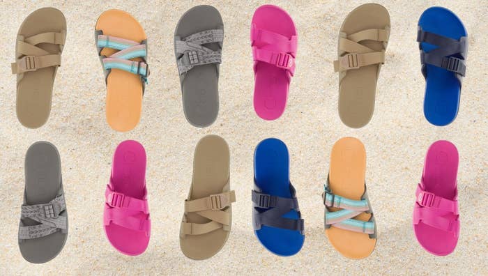 Berbagai gaya sandal yang diatur dengan latar belakang berpasir, menampilkan banyak warna dan desain tali untuk belanja alas kaki kasual