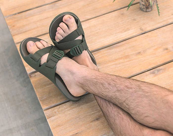Orang yang mengenakan sandal bertali yang nyaman dengan gesper yang dapat disesuaikan, kaki bertumpu di permukaan kayu