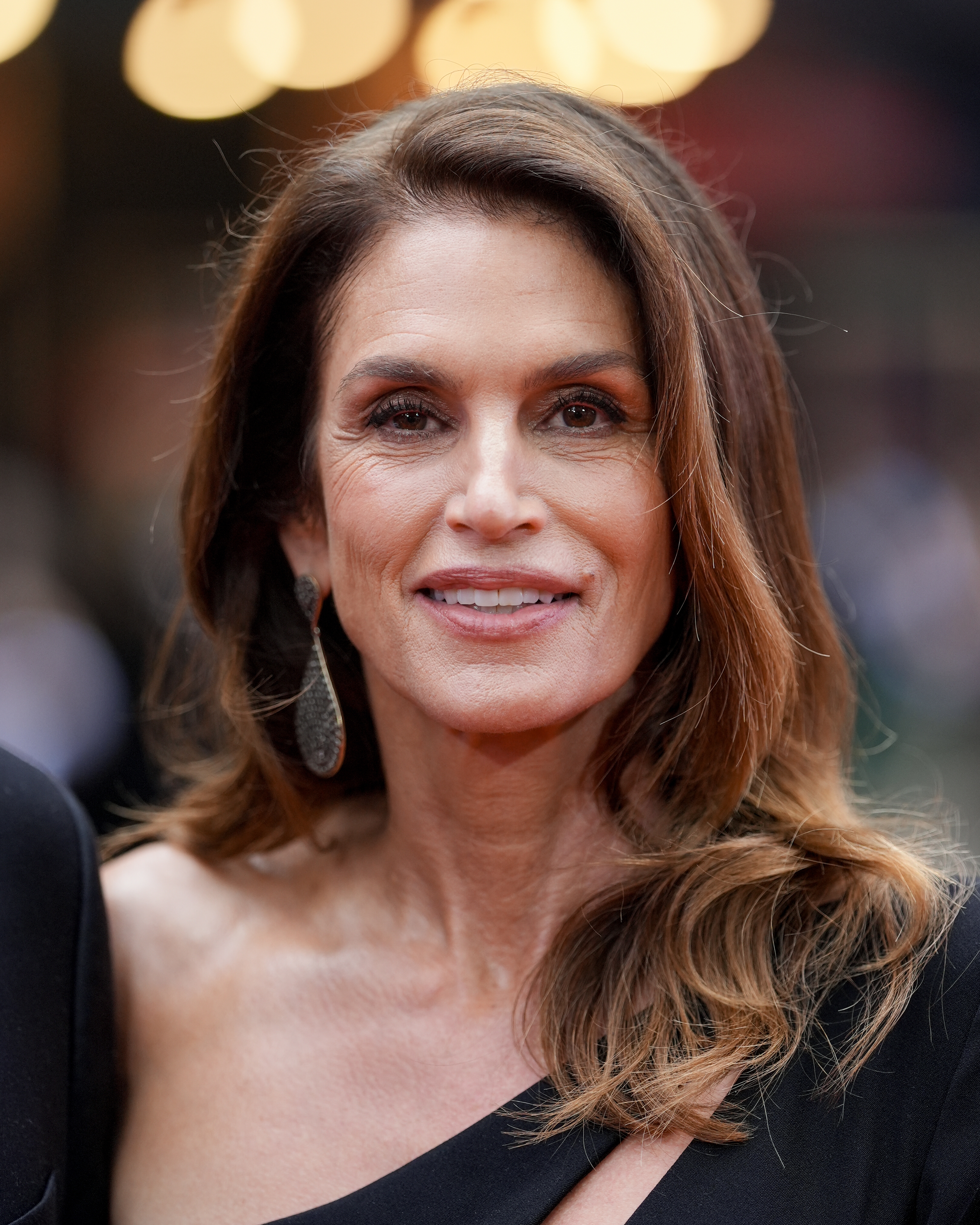 A woman on the red carpet in an elegant off-shoulder dress with long earrings, smiling at the camera