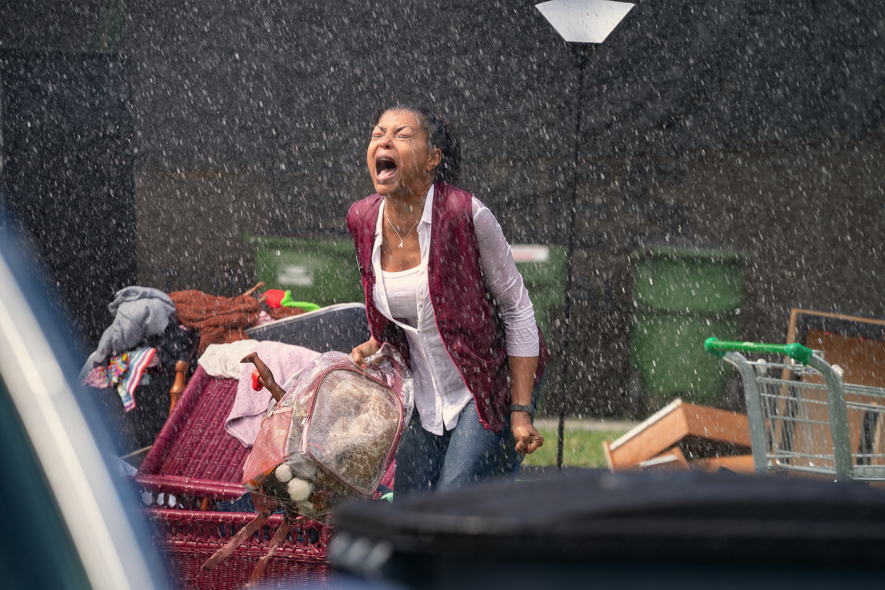 Person standing in the rain, emotionally yelling, surrounded by grocery carts and clothes, conveying intense drama