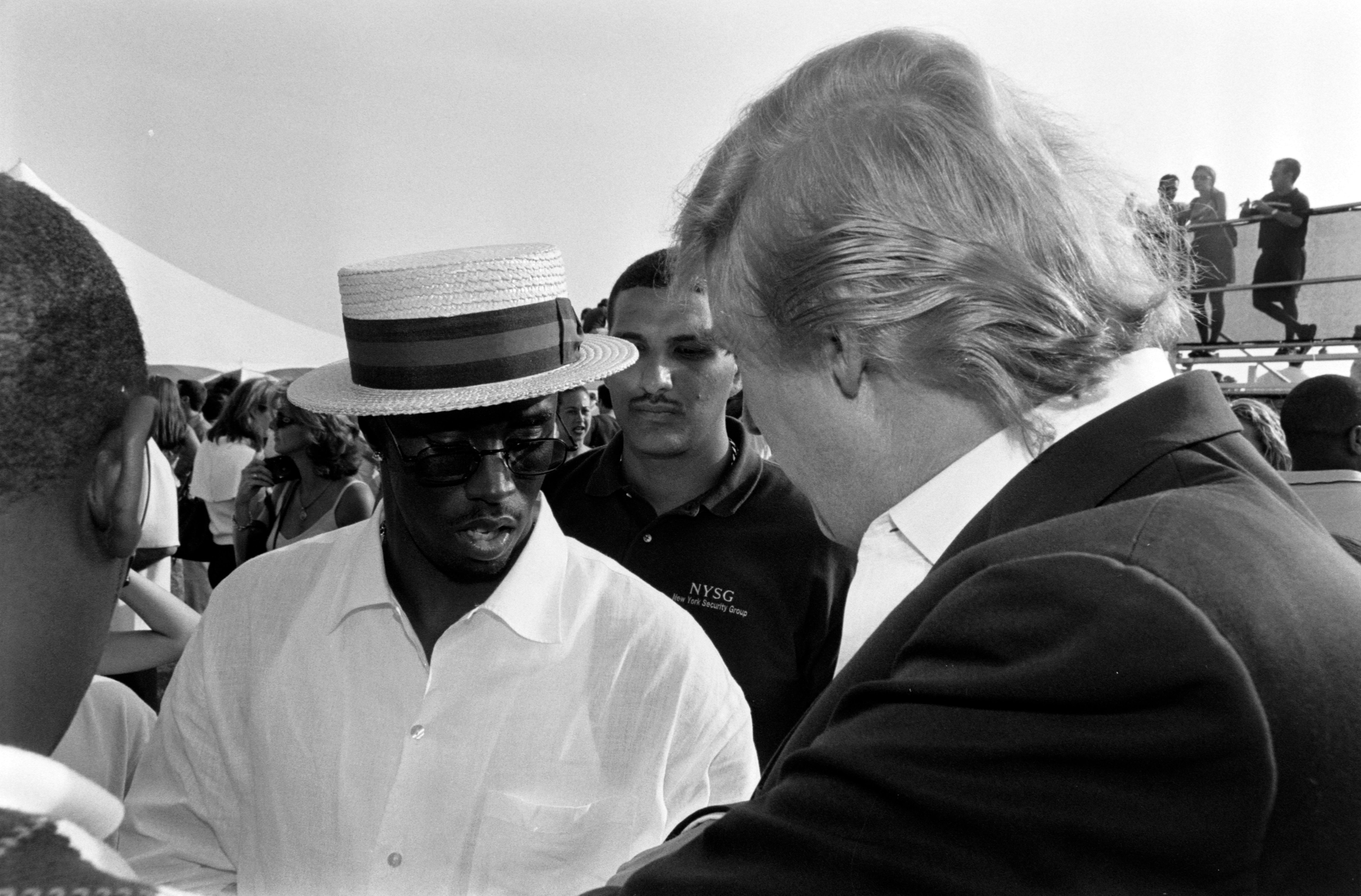 Diddy and Trump engaged in conversation at an outdoor event. One wears a straw hat and casual shirt; the other is in a suit
