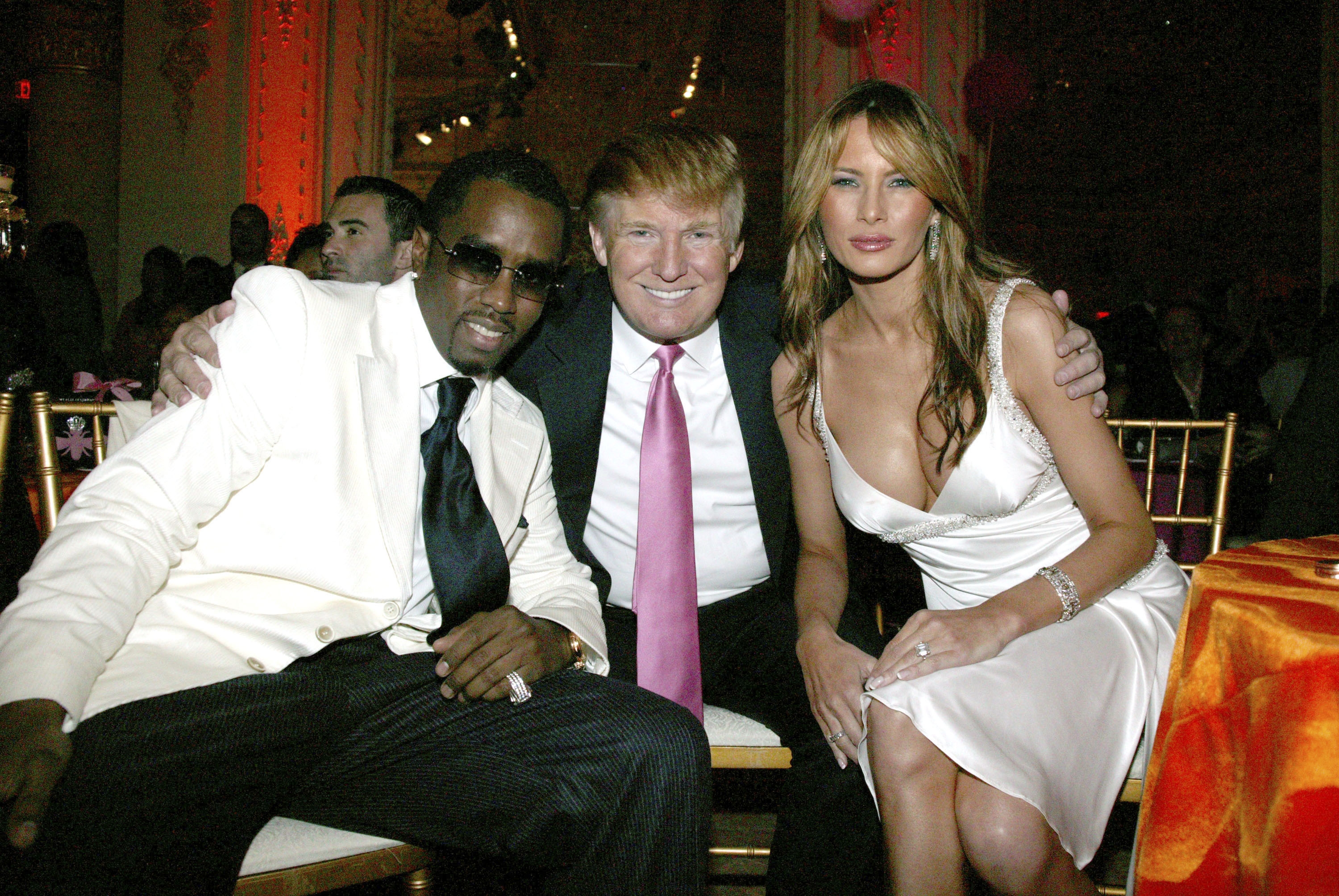 Diddy, Donald Trump, and Melania Trump seated at an event, with one in a black suit and white jacket, one in a suit with a pink tie, and one in a white dress