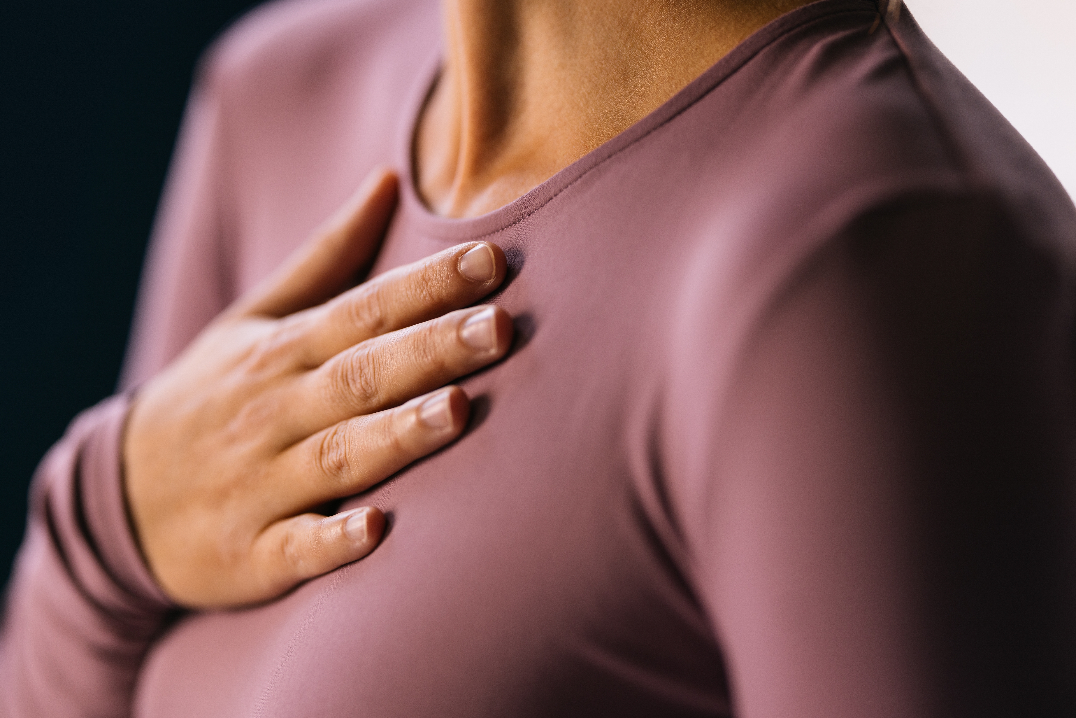 En person legger forsiktig hånden på brystet mens han har på seg en enkel, langermet topp