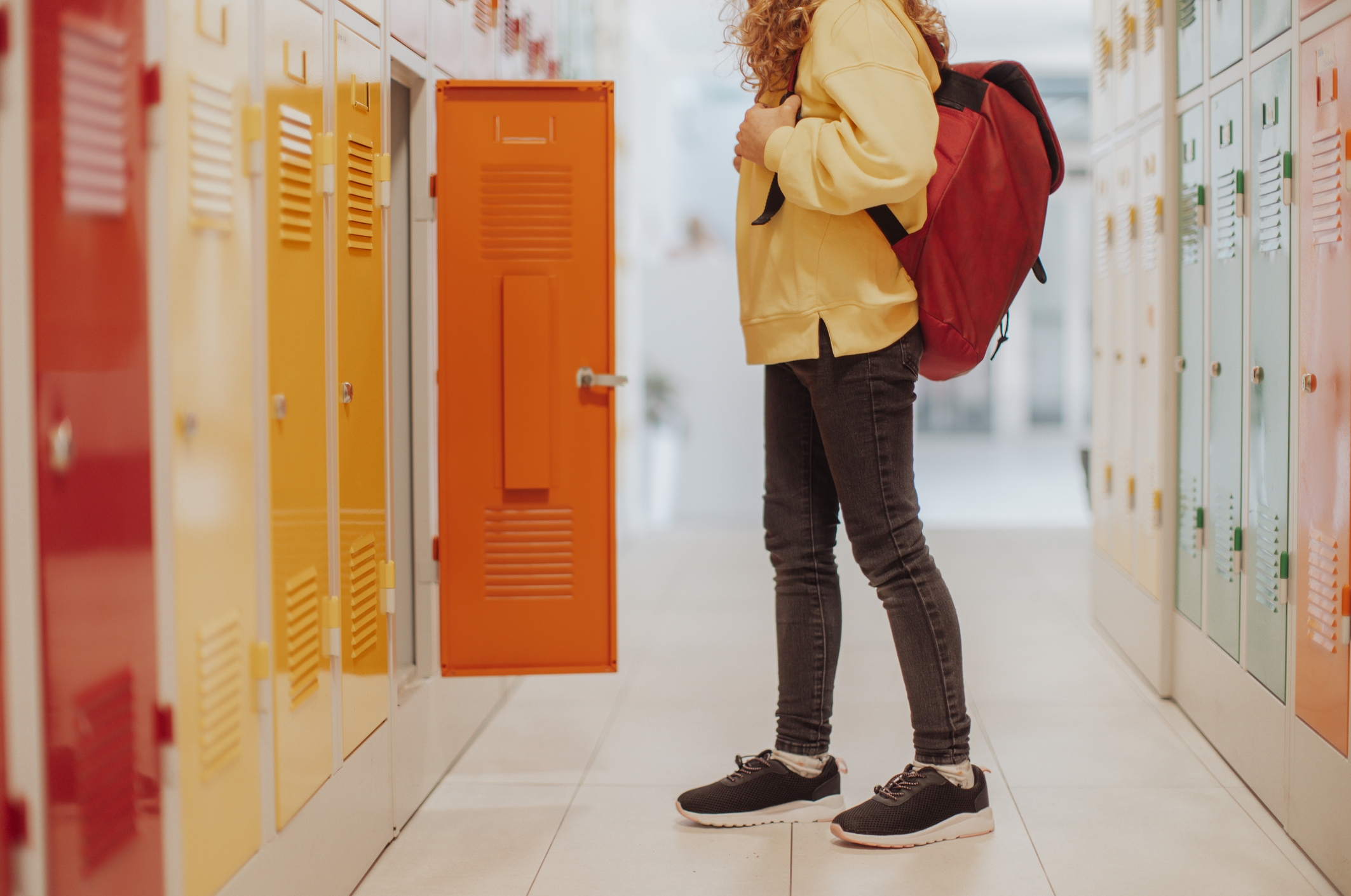 A student stands in a school hallway with their backpack, opening a locker surrounded by rows of other lockers