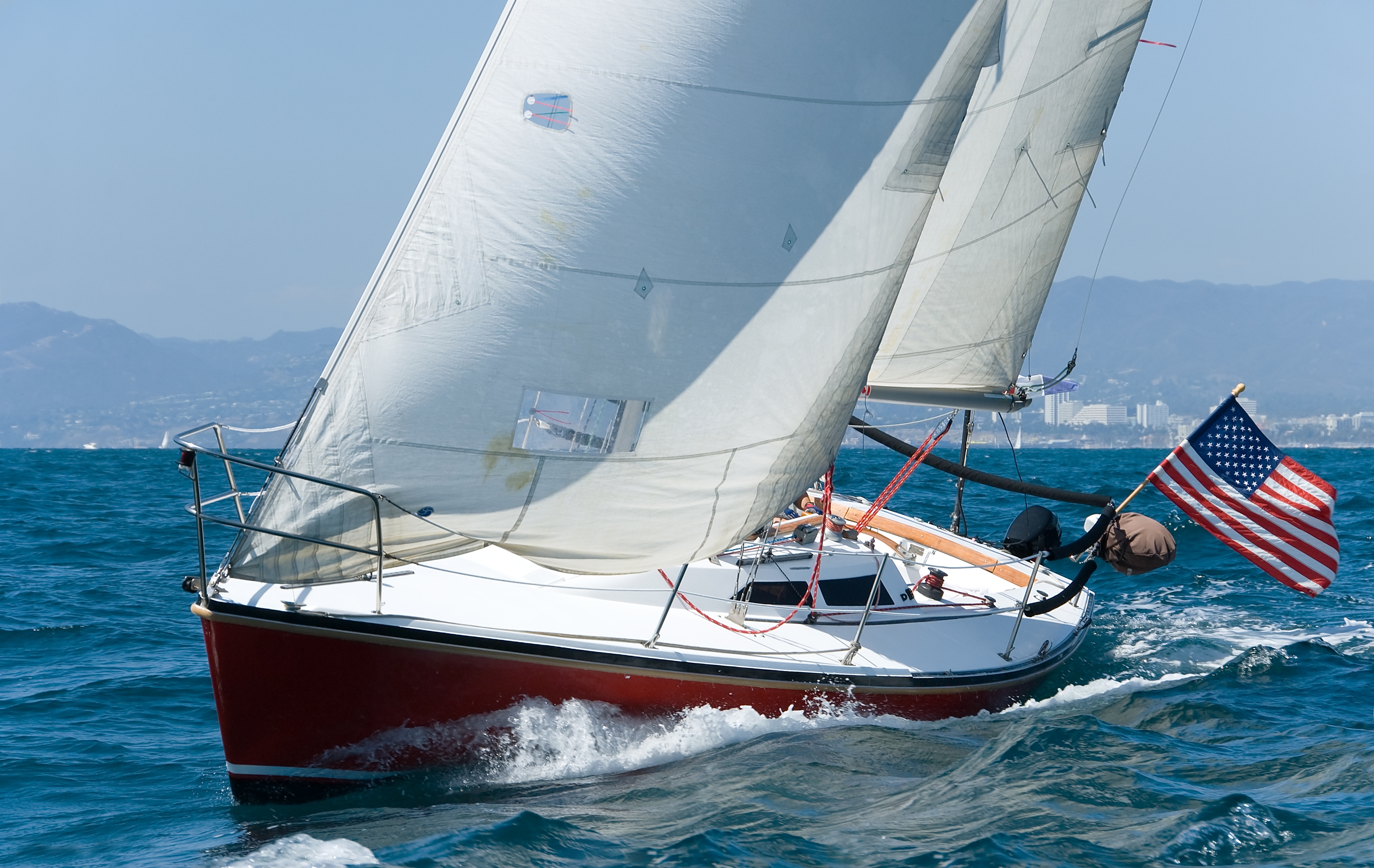 Sailboat with American flag gliding on ocean. Hills visible in the background