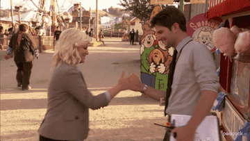 Two people enthusiastically high-five at a fairground, surrounded by playful attractions and cotton candy