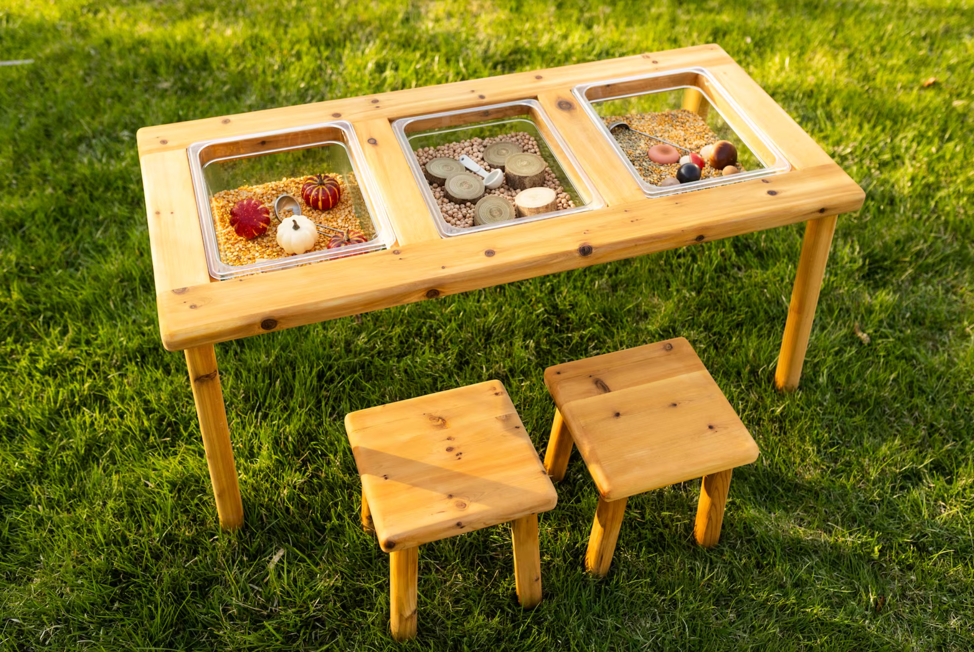 Wooden sensory table with three bins containing natural items and two small stools