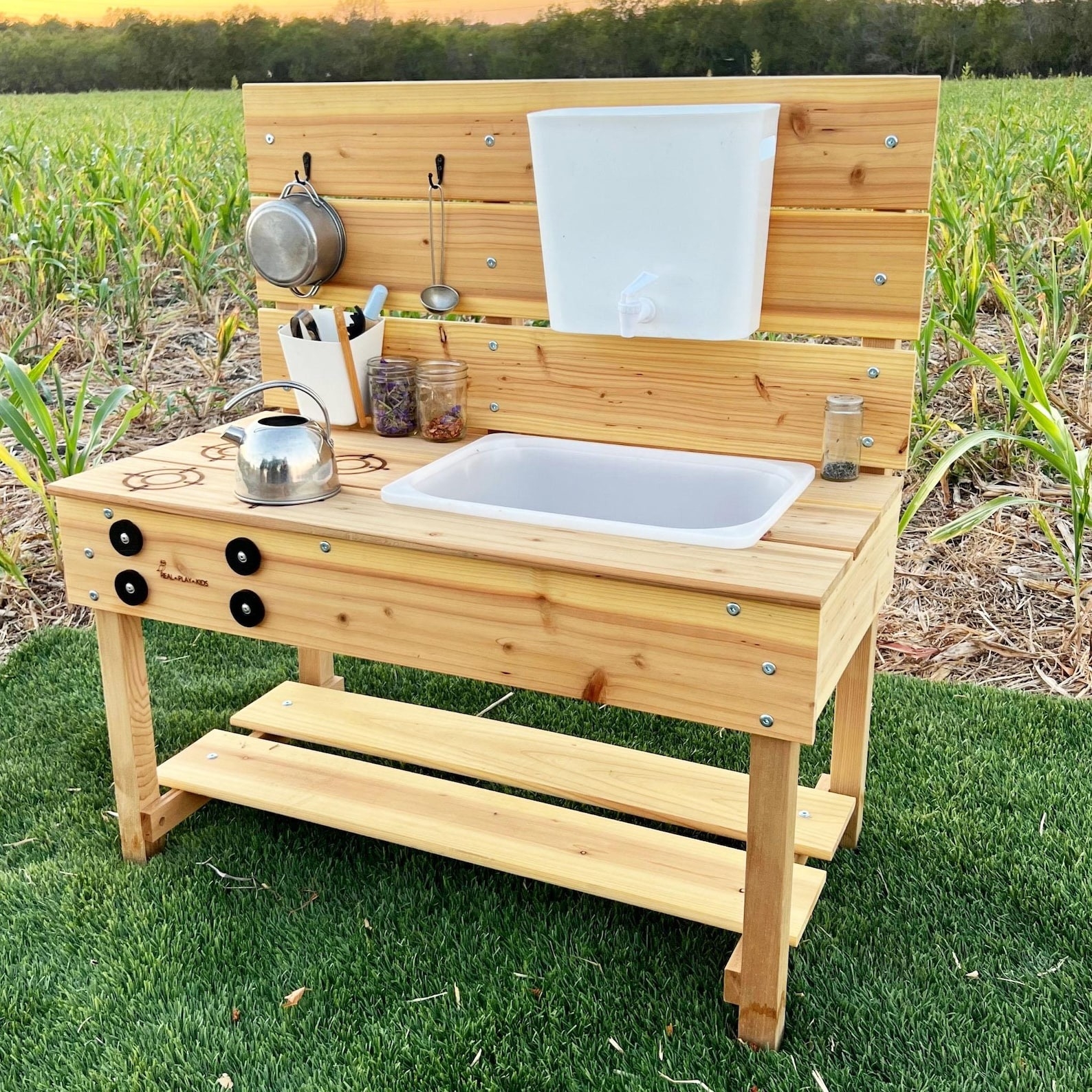 Wooden outdoor play kitchen set with sink, burners, and utensil hooks
