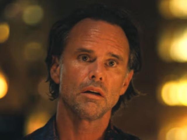 A man with medium-length hair looks concerned in a softly lit environment