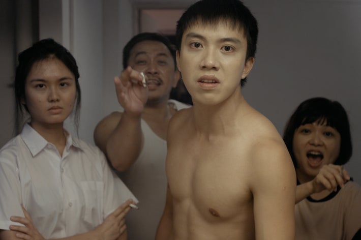 上半身裸の若い男性が、驚いた表情で立っている。後ろには3人の人々がいる。