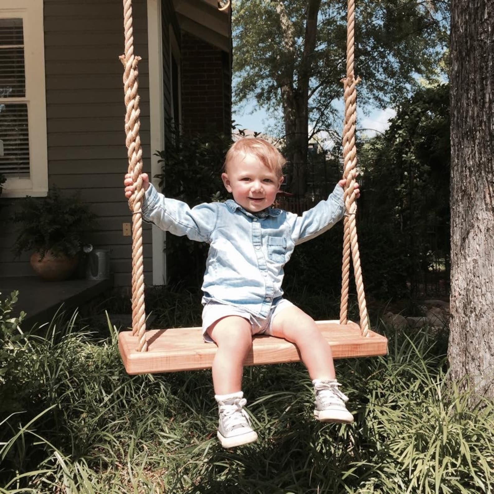 Toddler sitting on a wooden swing in a garden