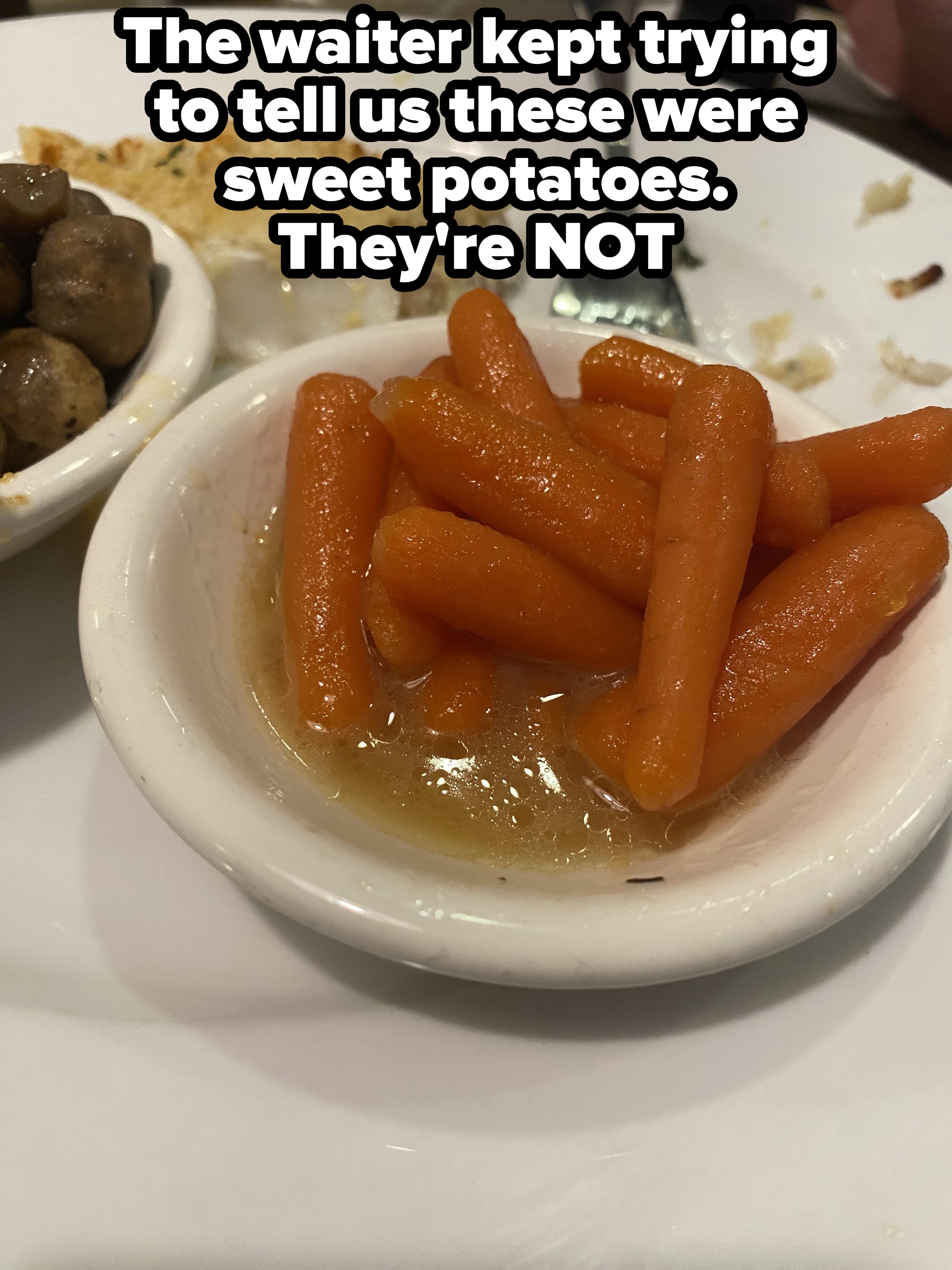 Plate of glazed baby carrots next to a dish of mushrooms and a partially eaten piece of fish with a fork on the side