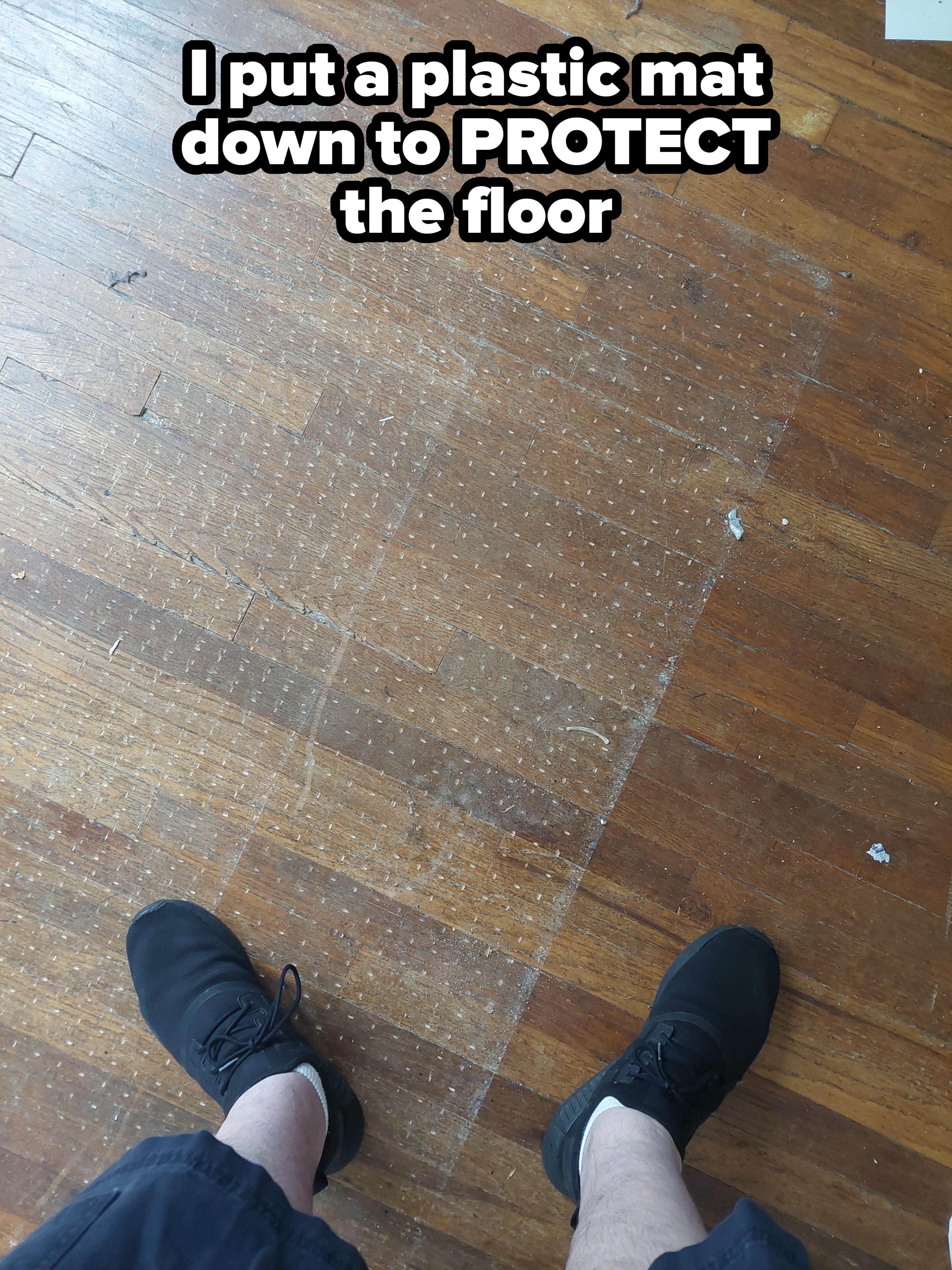 Person&#x27;s feet in black shoes standing on a wooden floor with a visible rectangular faded patch