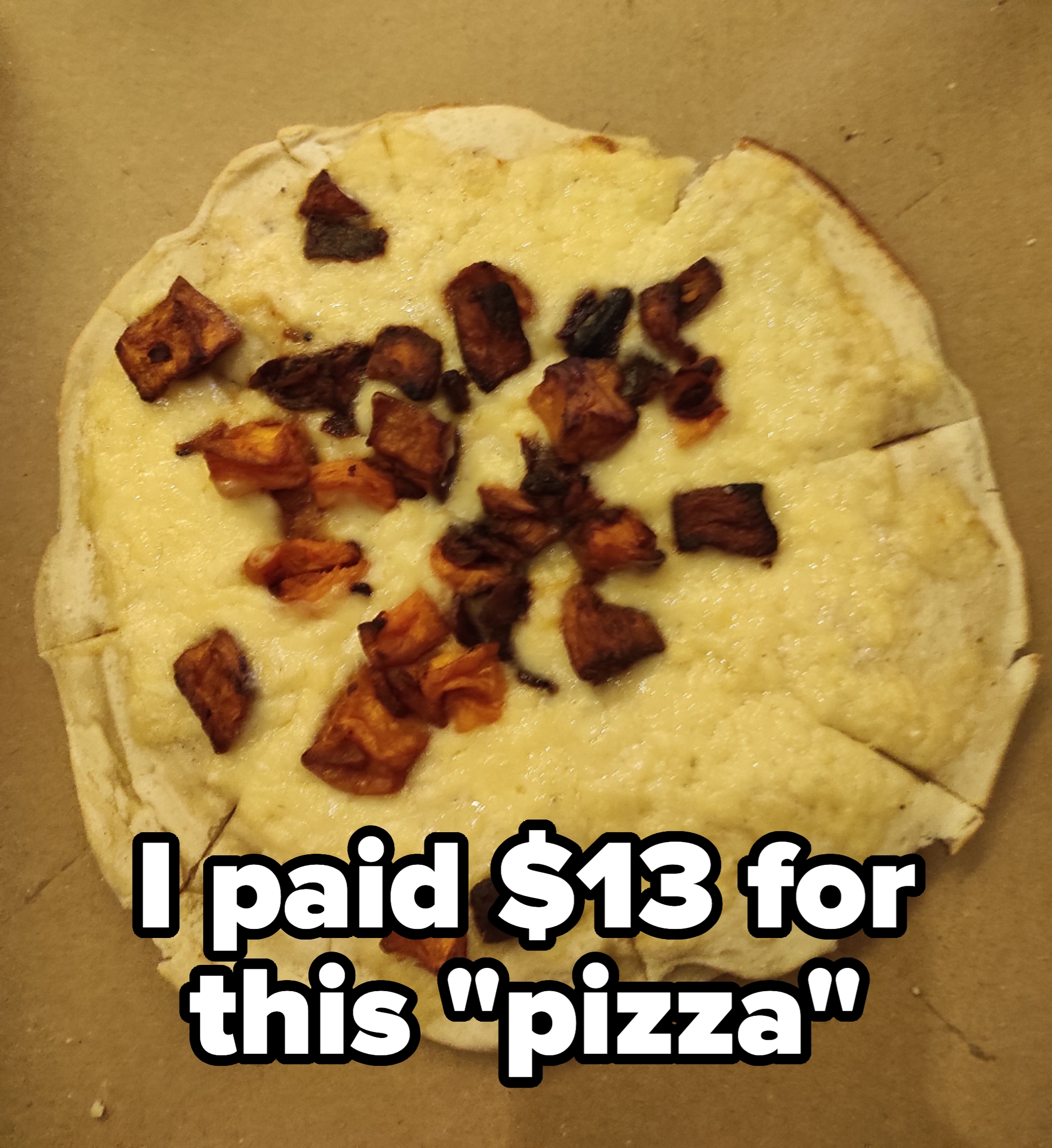 A pizza with melted cheese and scattered pieces of diced, roasted vegetables on a thin crust, cut into slices, placed on a cardboard surface