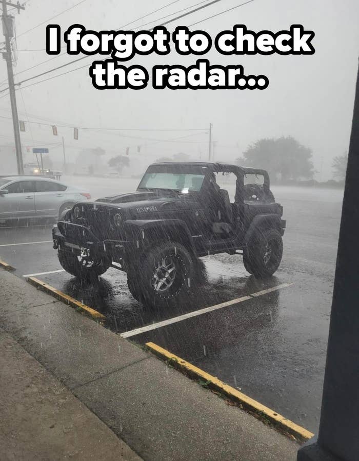 Jeep parked in a heavy rainstorm, with large off-road tires and no doors, in a mostly empty parking lot
