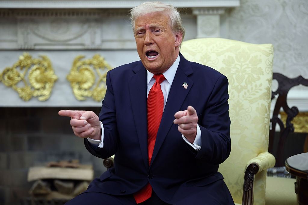 Person in a suit seated on an ornate chair, speaking passionately while making hand gestures