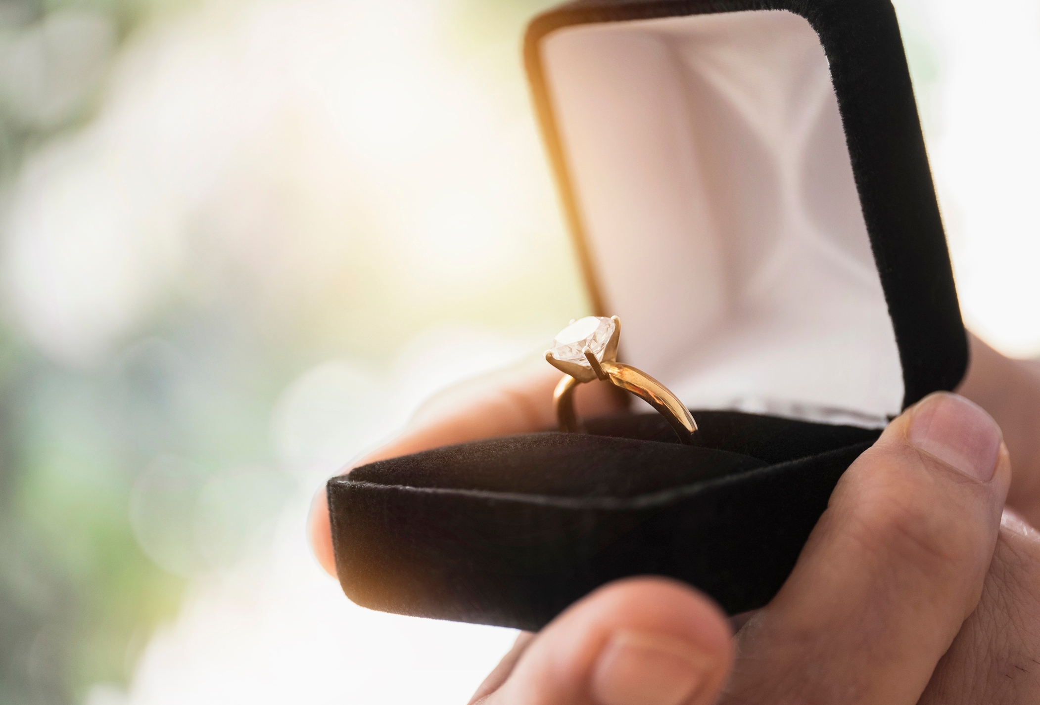 A hand holds an open ring box with a diamond engagement ring