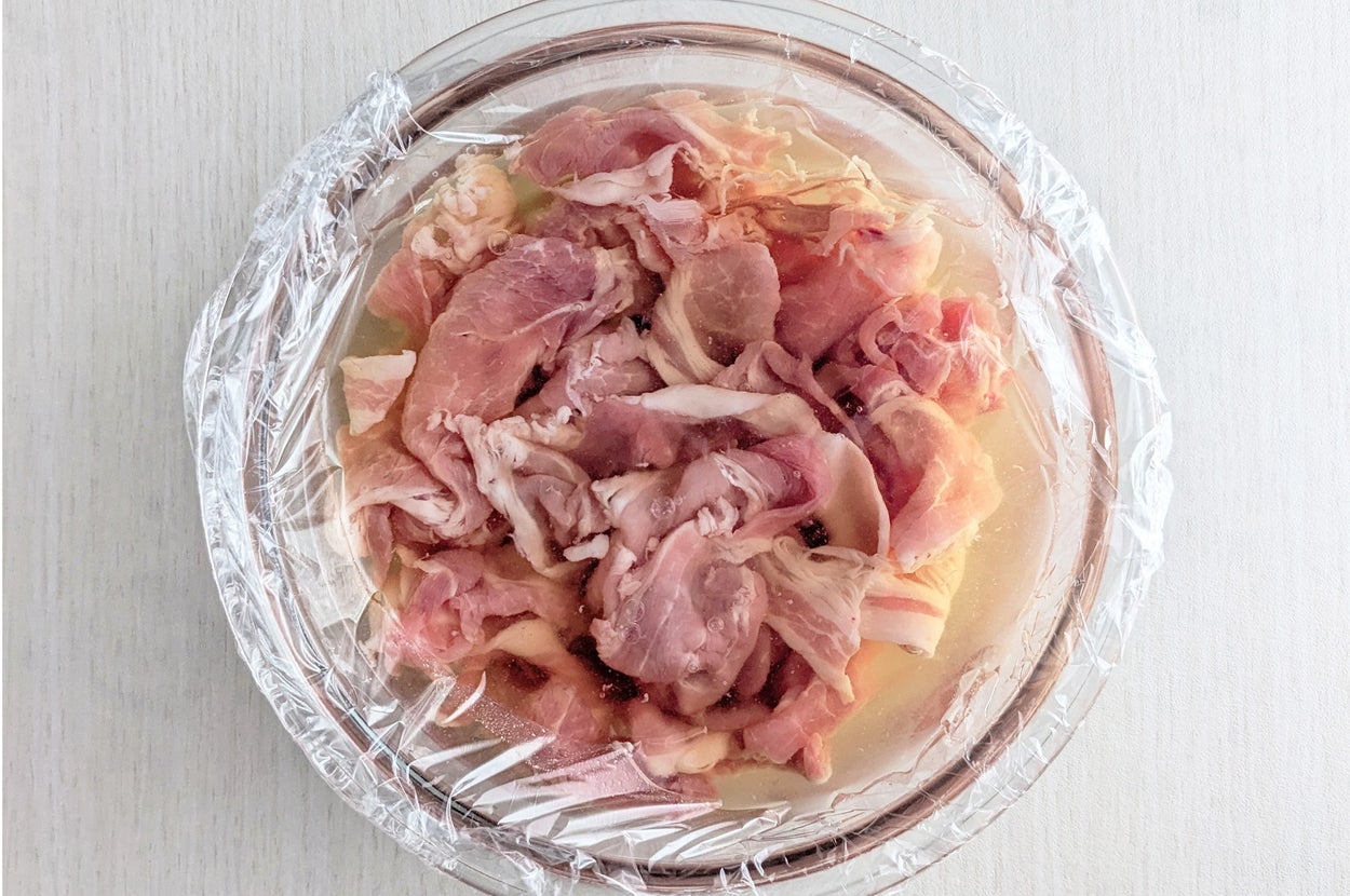 ラップで覆われたボウルに入った生の鶏肉。