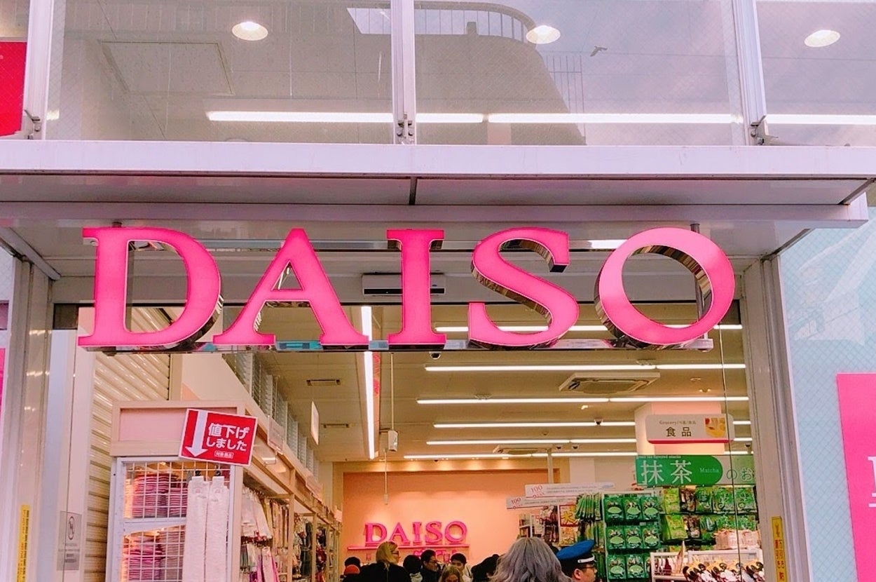多数の人が行き交うダイソー店舗の外観。入口上部に大きな「DAISO」の看板がある。