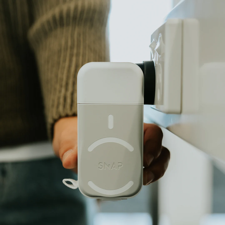Person plugging a compact, white air freshener into a wall outlet at home