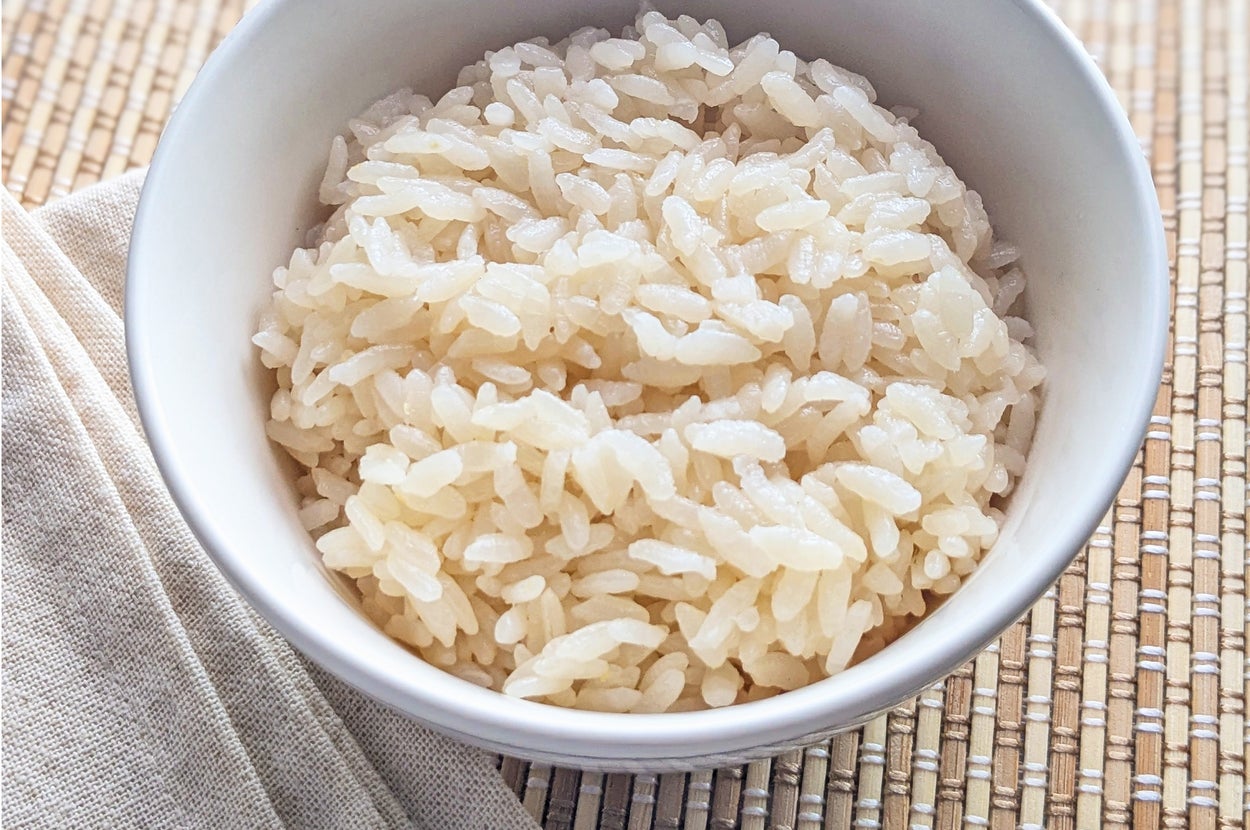 白い陶器のボウルに入った炊きたてのご飯。竹製のマットと箸が付属しています。