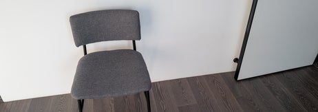 壁際に置かれたシンプルな椅子と鍵が挿さったドア、木製床が見える室内。