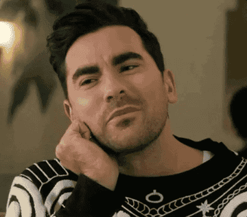 Person with short dark hair, wearing a patterned sweater, has a thoughtful expression, resting their hand on their cheek