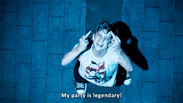 Person in sneakers and casual outfit stands outside at night, smiling, with a playful expression, gesturing upwards. Text: &quot;My party is legendary!&quot;