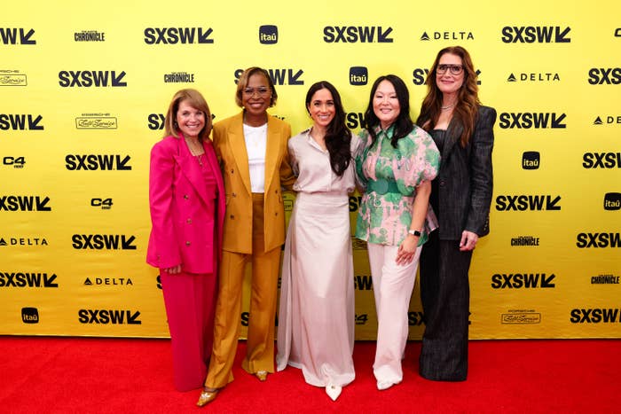 Five women pose on a red carpet at SXSW; they wear stylish suits and elegant dresses