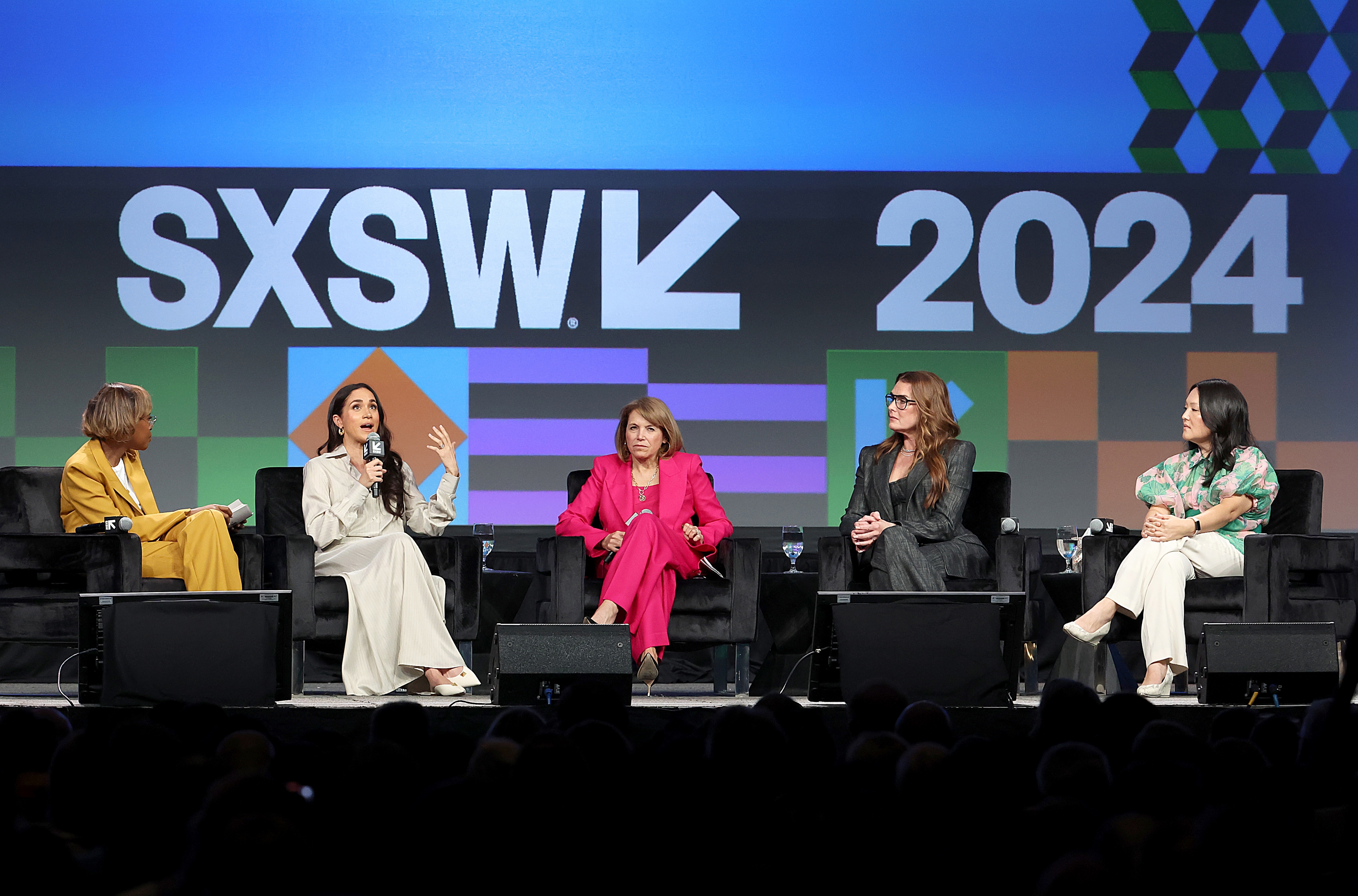 Five people in stylish outfits on a panel discussion at SXSW 2024, seated on stage with microphones, engaging with the audience