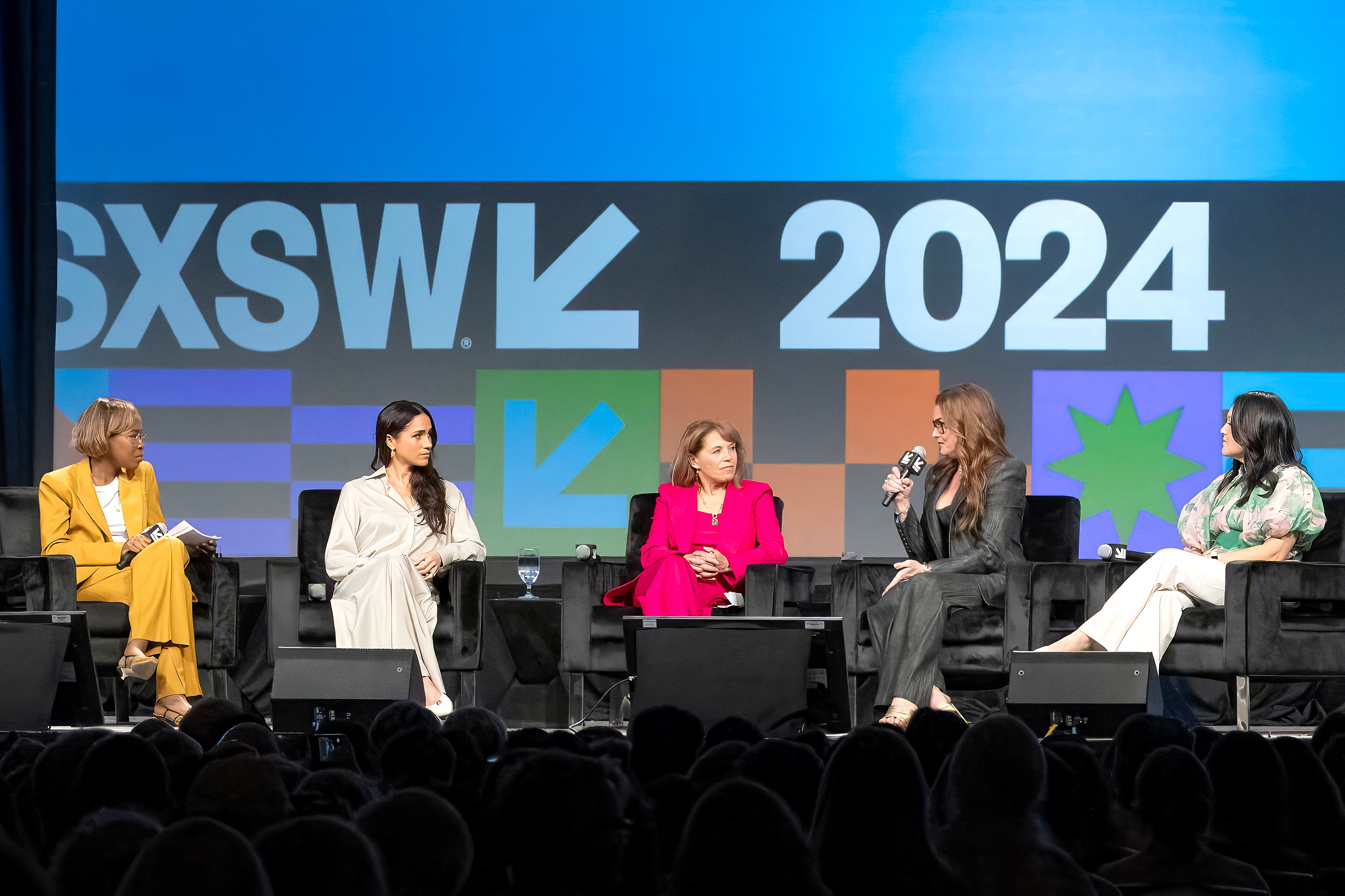 Five women in business attire are seated on a stage, engaged in a discussion at an event with "SXSW 2024" displayed in the background