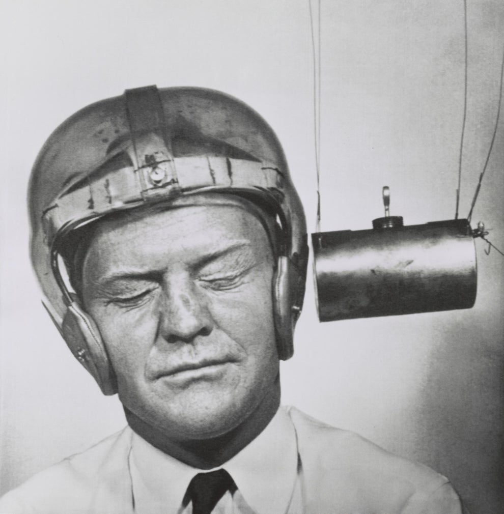 A person wearing a helmet with eyes closed, facing a cylindrical object hanging beside them