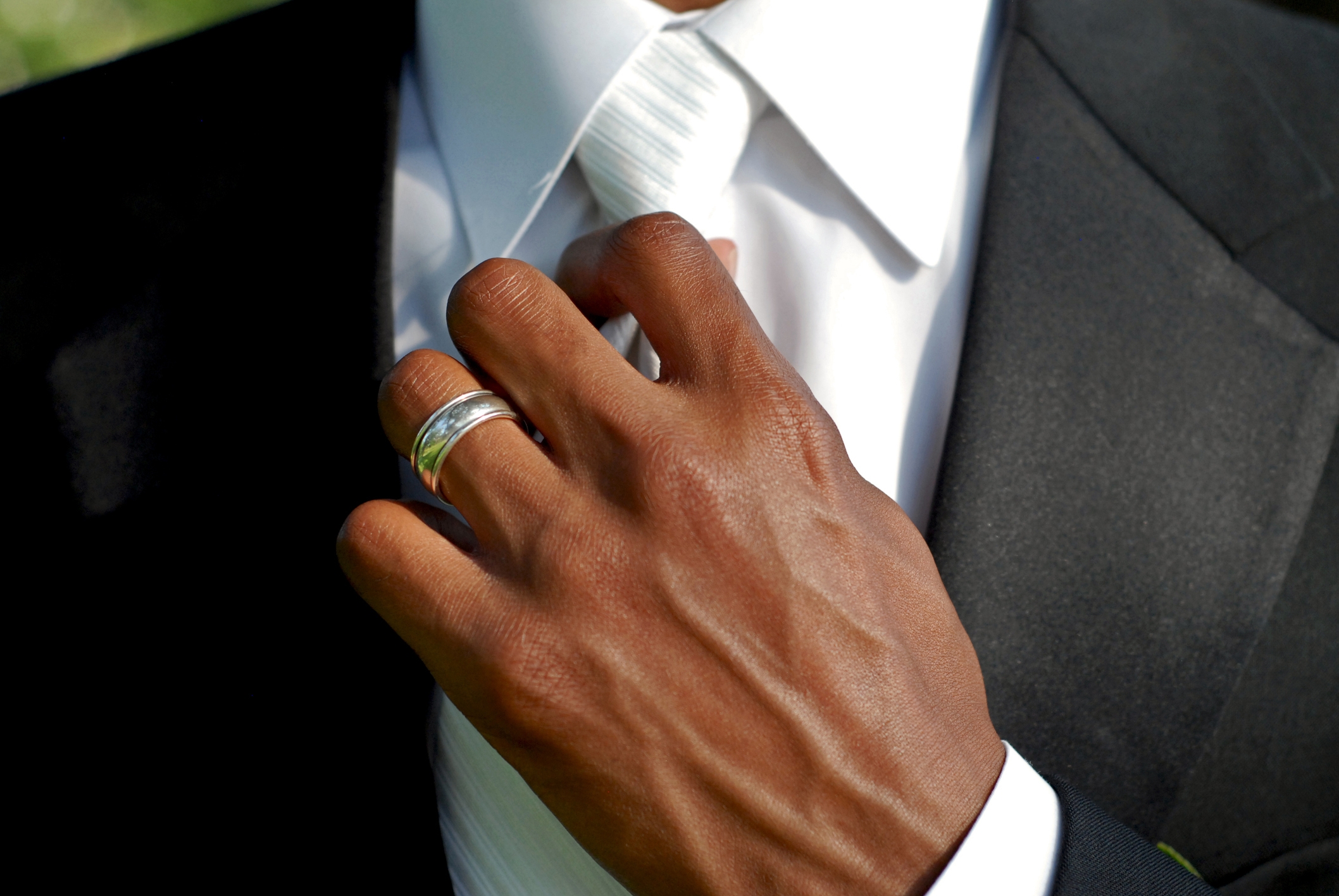 Close-up of a person adjusting a tie and wearing a suit, showcasing a silver ring on their finger