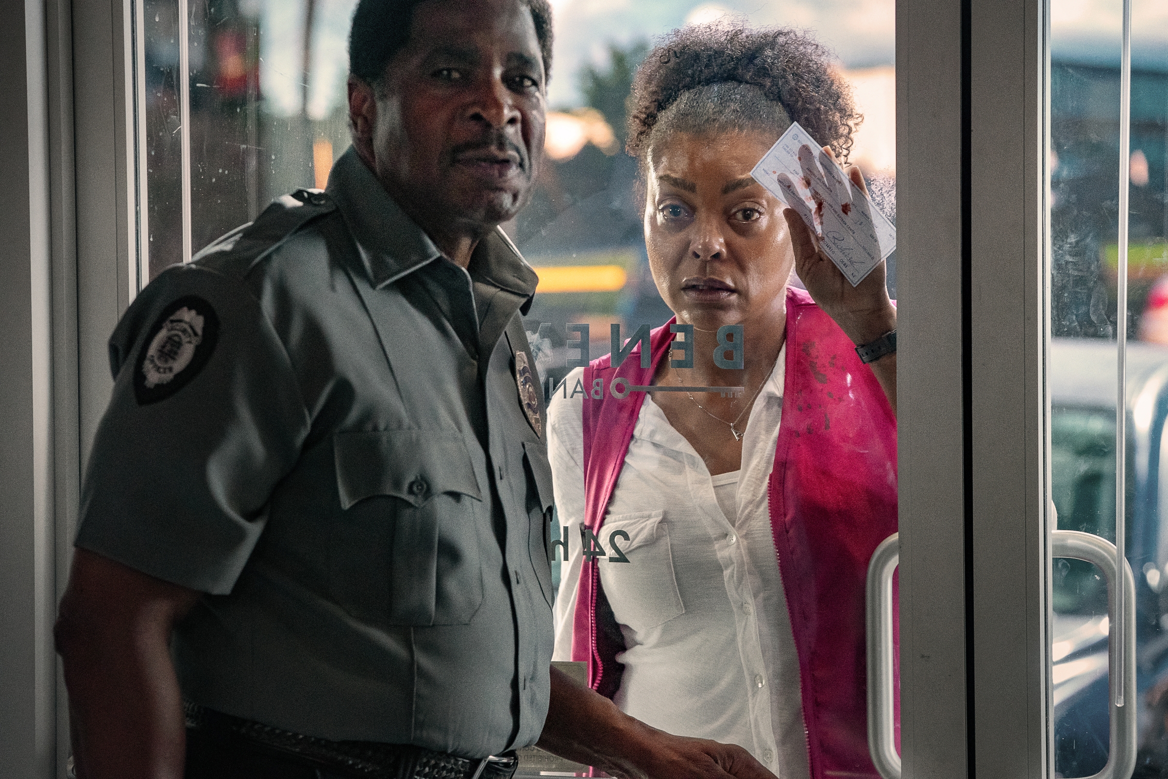 Two concerned individuals peek through a glass door, the woman holds papers and looks anxious