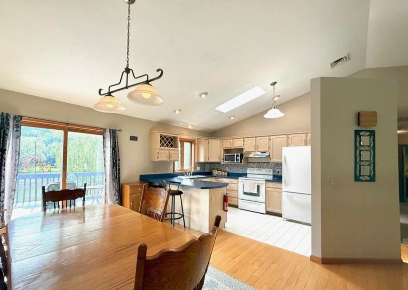 Spacious room  and eating  country  with woody  table, chairs, and modern   appliances. Large model   offers a presumption    of greenery and a balcony