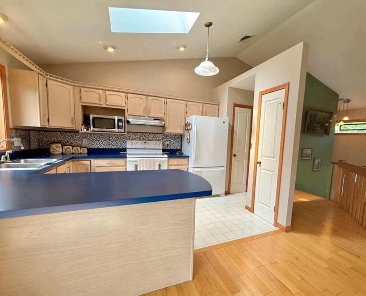 Spacious room  with woody  cabinets, bluish  countertops, and a achromatic  fridge. A skylight and assorted  tiny  appliances are visible