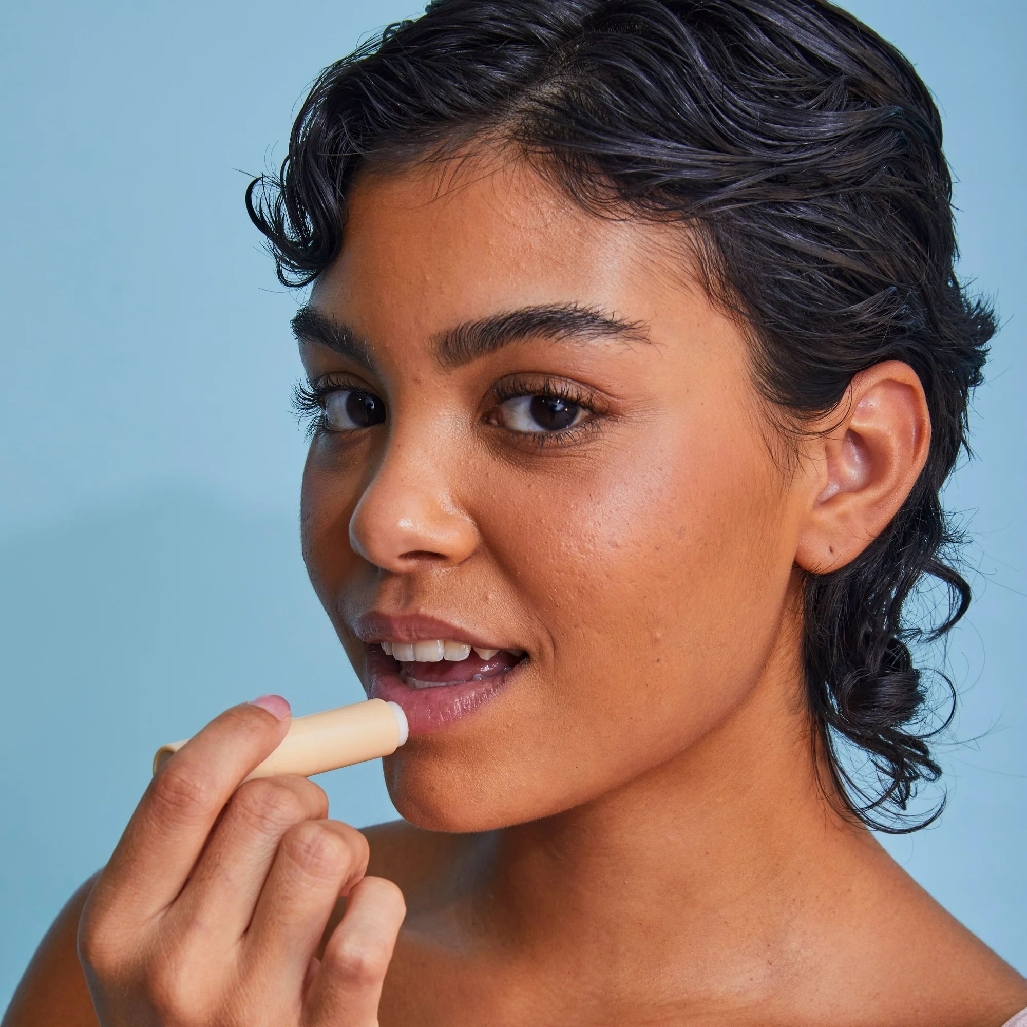 Person applying articulator  balm to their lips, holding the merchandise  successful  a light-colored conduit  against a plain background