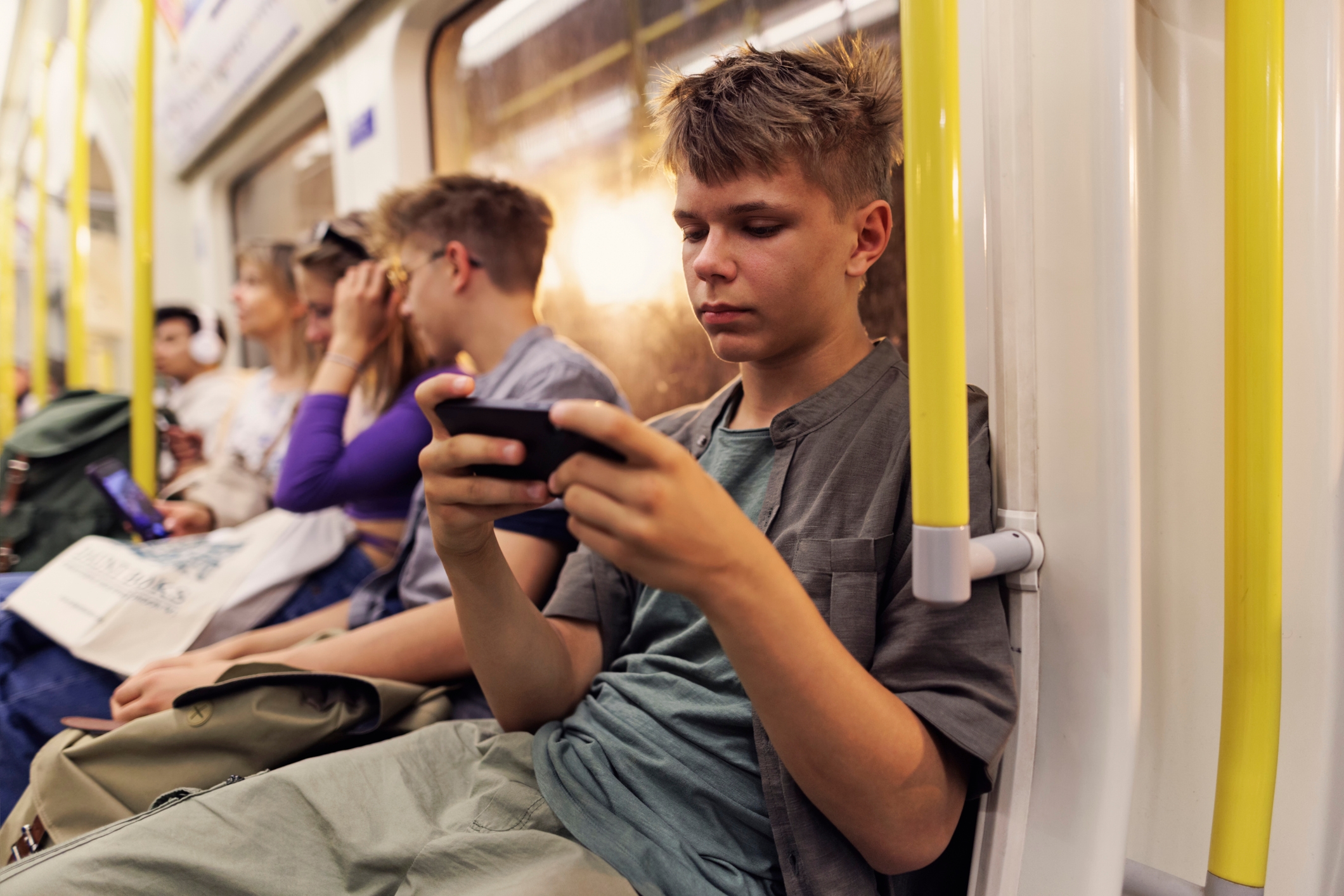 Tenåring fokuserte på telefon mens du sitter på et tog, andre sitter i nærheten engasjert med enheter, rolig pendlingsatmosfære