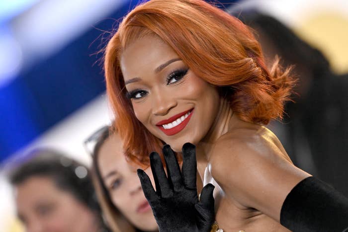 Keke Palmer smiling and waving, wearing a sleeveless outfit with long gloves at a formal event