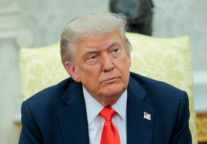 A person in a suit with an American flag pin sits in a formal setting, looking thoughtful