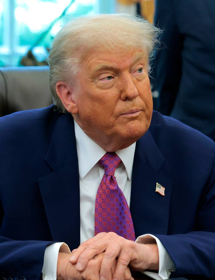 Donald Trump in a suit and patterned tie seated in an office, looking to the side with a thoughtful expression