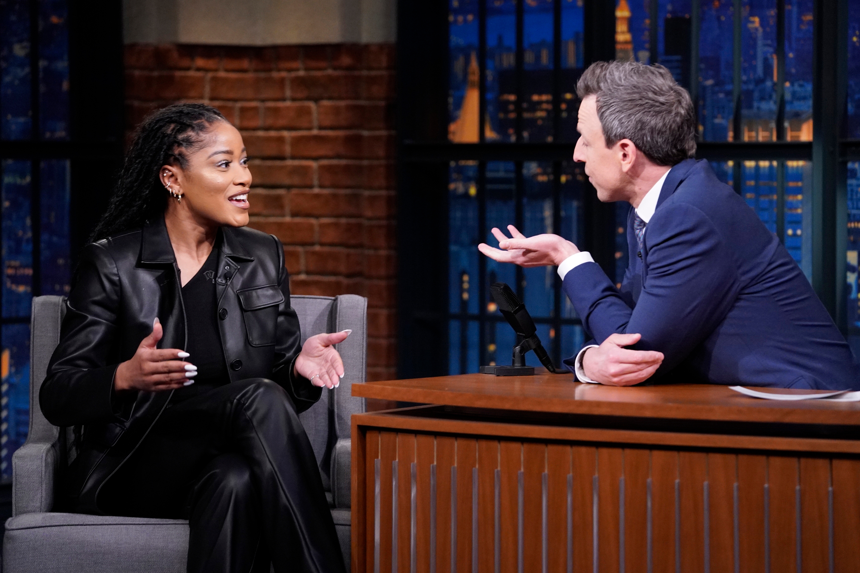 Keke Palmer in leather attire interviews with Seth Meyers on a talk show set